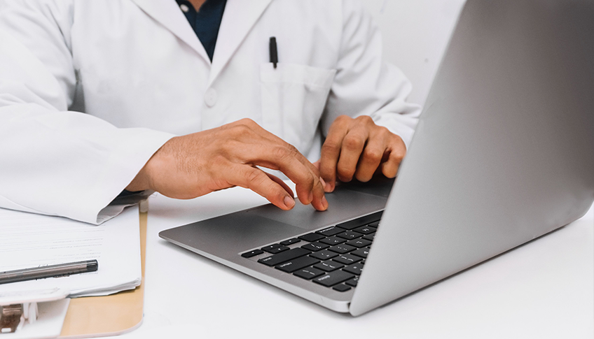 Medical professional typing on a laptop beside paper documents